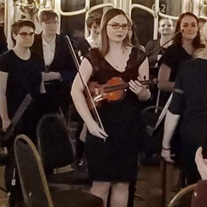 Hidden Talents - Becky With a Violin and Bow Surrounded by People and Chairs