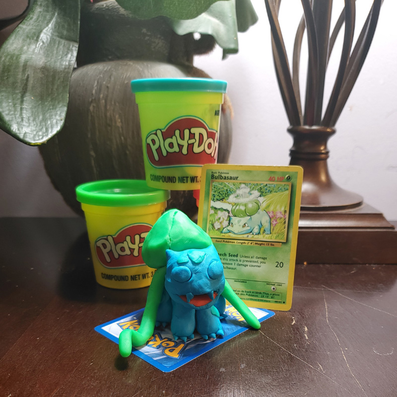 Hidden Talents - Containers of Play-Doh Stacked Next to Pokemon Card and Sculpture